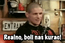 a man holding a microphone with the words realno boli nas kurac written below him