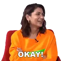 a woman in an orange sweater is sitting in a chair with her arms crossed and says okay