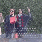 two women are standing next to each other and one is giving a peace sign while the other is holding a red bag .