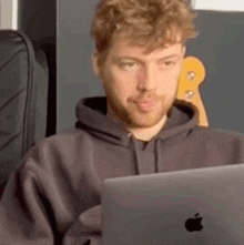 a man with a beard is sitting in front of an apple laptop computer .