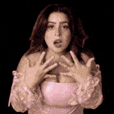 a woman in a pink top is making a surprised face with her hands on her chest