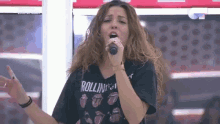 a woman singing into a microphone wearing a rolling stones shirt .
