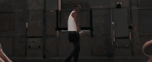 a man in a white tank top is standing in a room with naked people