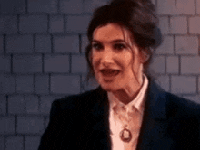 a woman in a suit is standing in front of a brick wall and making a funny face .