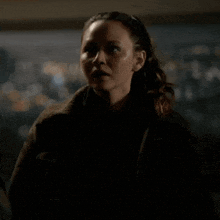 a woman in a black jacket is standing in a dark room looking at the camera .
