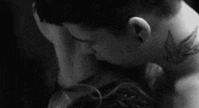 a man and woman are kissing in a black and white photo . the woman has a tattoo on her neck .