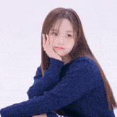 a girl wearing a blue sweater has her hand on her chin