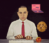 a man is typing on a keyboard with an apple and a cookie in front of him