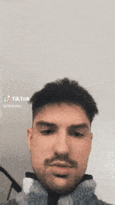 a man with a beard and mustache is taking a selfie with a tiktok app .