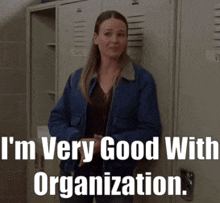 a woman in a blue jacket is standing in front of lockers with the words i 'm very good with organization