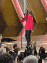 a man in a red jacket is speaking into a microphone in front of a crowd