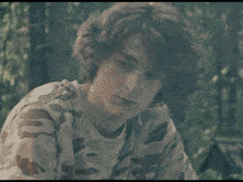 a young man wearing a camouflage shirt is looking at the camera