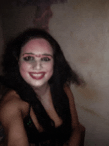 a woman with makeup on her face is smiling in a dark room .