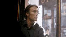 a man in a black shirt looks out a window in front of a sign that says ' op '
