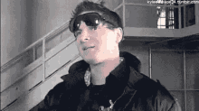 a man wearing sunglasses and a black jacket is standing in a room .