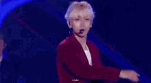 a man is standing on a stage with his arms outstretched and wearing a red shirt .