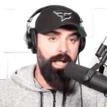 a man with a beard is wearing headphones and a hat and talking into a microphone .