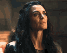 a woman with long dark hair and blue eyes is wearing a black leather jacket .