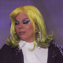 a woman wearing a yellow wig and hoop earrings looks at the camera
