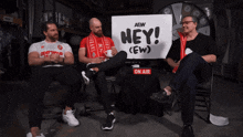 three men are sitting in front of a sign that says hey ( ew )