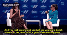 two women are sitting in chairs talking to each other while one of them is holding a microphone .