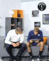 two men sitting on a couch with a sign that says mbappe live on it