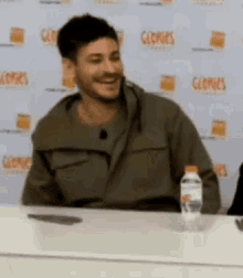 a man is smiling while sitting at a table with a bottle of water .