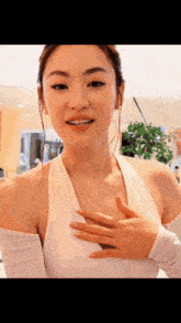 a woman in a white top is smiling and holding her hand to her chest