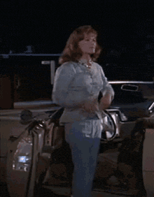 a woman in a blue shirt is standing next to a car at night