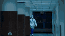 a man in a lab coat is walking down a hallway with an exit sign on the wall