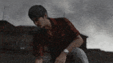 a man in a red shirt with a watch on his wrist is kneeling down in the rain