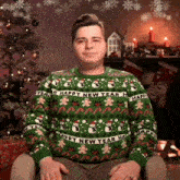 a man wearing a green sweater that says happy new year is sitting in front of a christmas tree