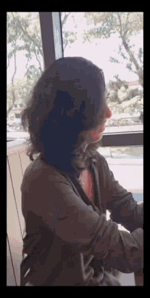 a woman with long hair is sitting in front of a window with trees in the background