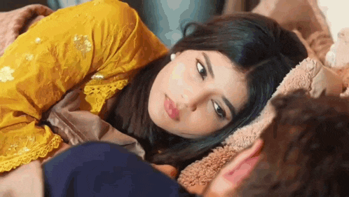 a woman in a yellow dress is laying on top of a man in a bed .