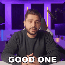 a man with a beard says good one while sitting in front of a microphone