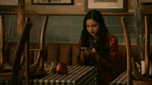 a woman sits at a table with a checkered tablecloth looking at her phone