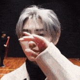 a man with white hair is covering his face with his hands .