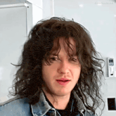 a man with long curly hair is wearing a denim jacket and black shirt