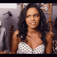 a woman wearing a polka dot top and hoop earrings makes a funny face
