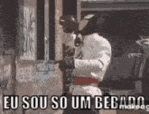 a man in a karate uniform is standing in front of a building with a sign that says eu sou so um bebado