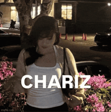 a woman in a white tank top is standing in front of pink flowers with the name chariz written on the bottom