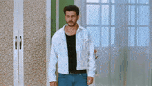 a man in a white jacket and blue jeans stands in front of a wardrobe