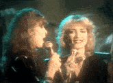 two women singing into microphones one of whom has a ring on her finger