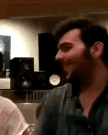 a man with a beard is talking to another man in a room with speakers in the background .