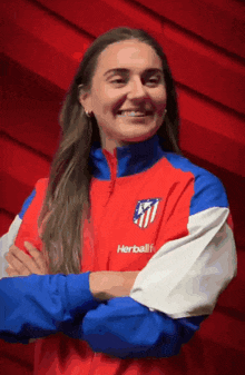 a woman wearing a red , blue , and white jacket with her arms crossed is smiling .