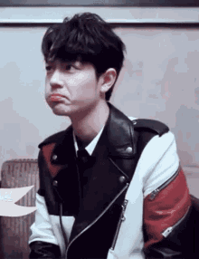 a young man is making a funny face while wearing a leather jacket .