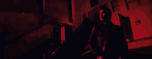 a man in a black jacket is holding a gun in front of a building at night .