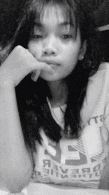 a black and white photo of a young woman with her hand on her face .