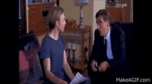 two men are sitting on a couch talking to each other . one of the men is holding a piece of paper .