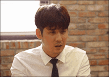 a man in a white shirt and tie is sitting in front of a brick wall with his mouth open